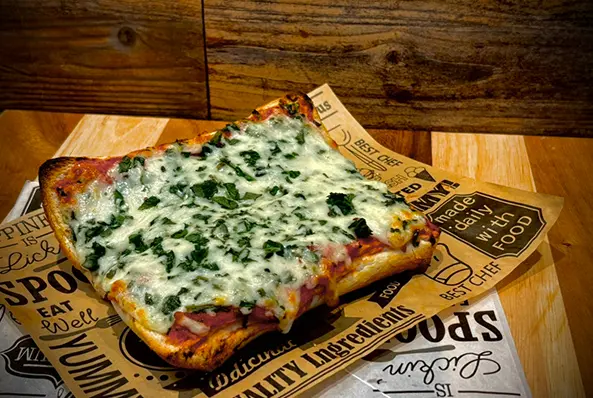 Cheesy spinach pizza slice on wooden table.