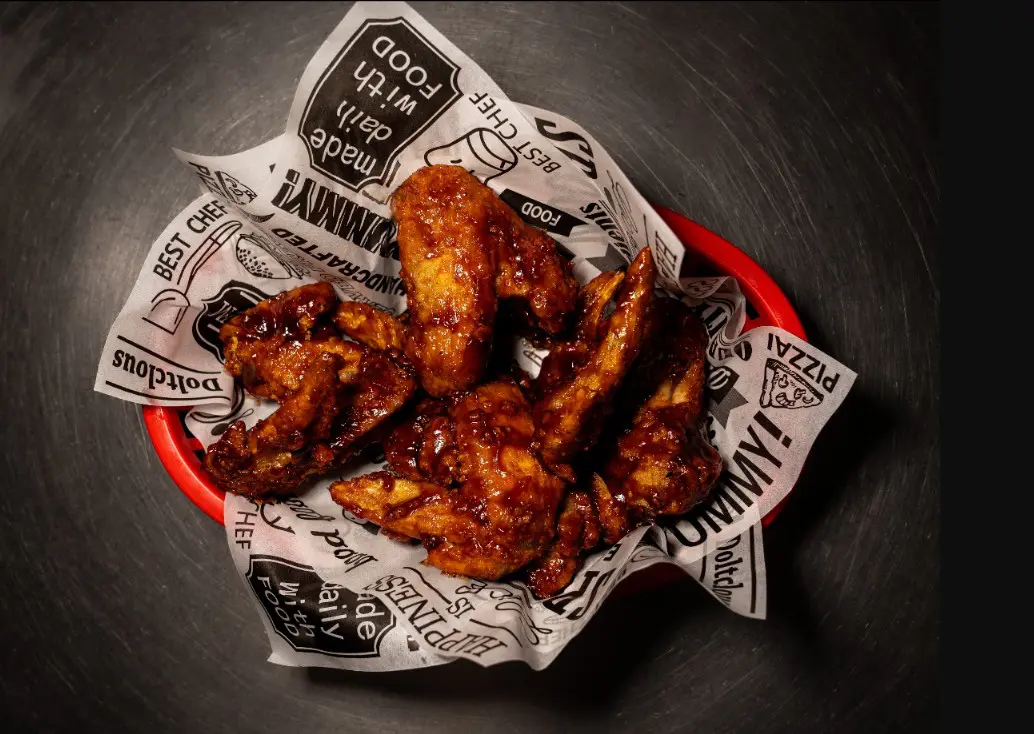 Basket of saucy chicken wings on paper.
